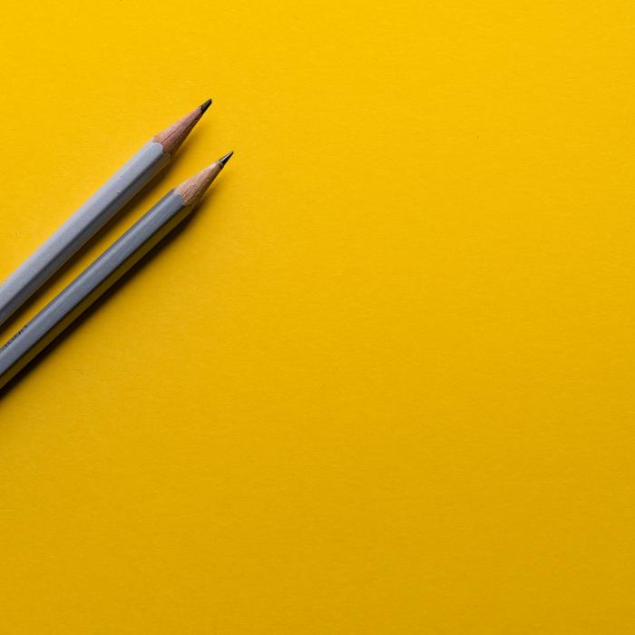 A dark yellow background with two grey pencils partially visible on left hand side of picture