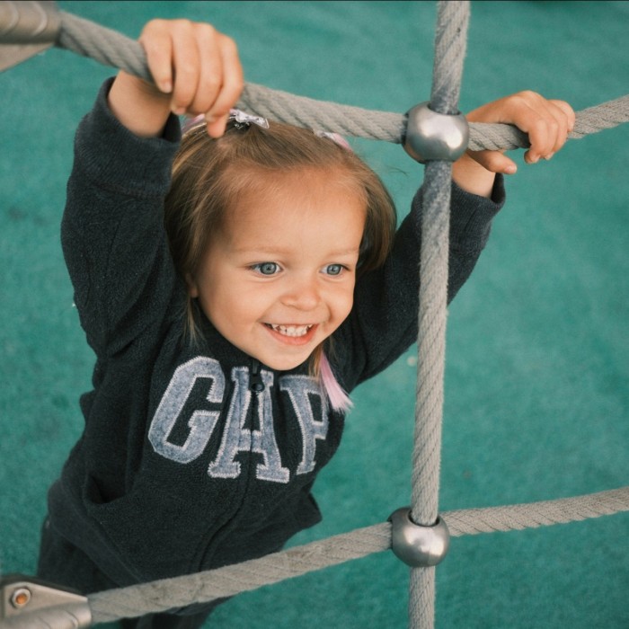 Little girl at play hanging onto a cargo net