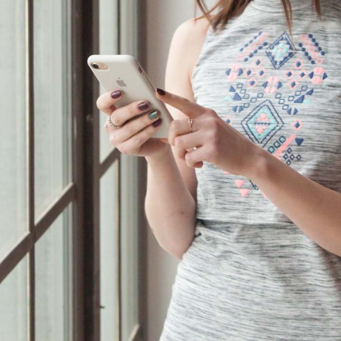 Young woman using her mobile phone while standing next to a large window